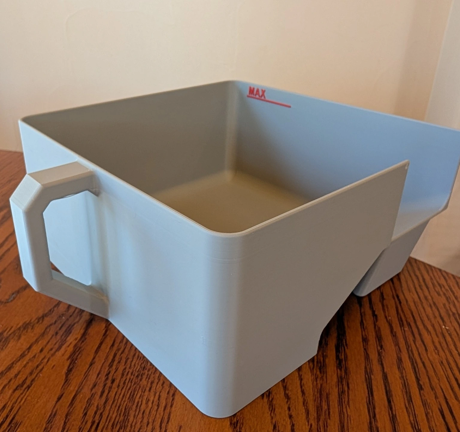 Gray 3D printed open collection bin with an integrated side handle and red MAX fill-level marker, on a wooden table