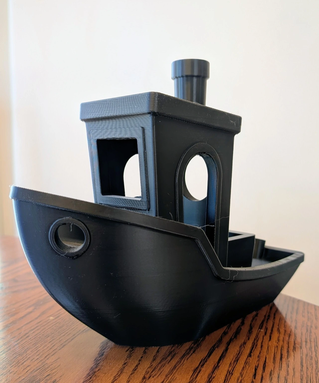 Aaron’s black 3D printed boat photographed on a wooden table, showing the hull, cabin openings, and chimney